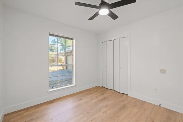 an empty room with wooden floor fan and windows