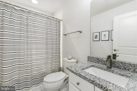 a bathroom with a granite countertop toilet a sink a mirror and shower curtain