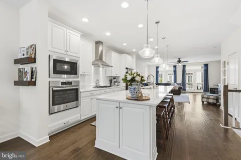 a kitchen with stainless steel appliances kitchen island granite countertop a stove a sink a refrigerator and white cabinets with wooden floor