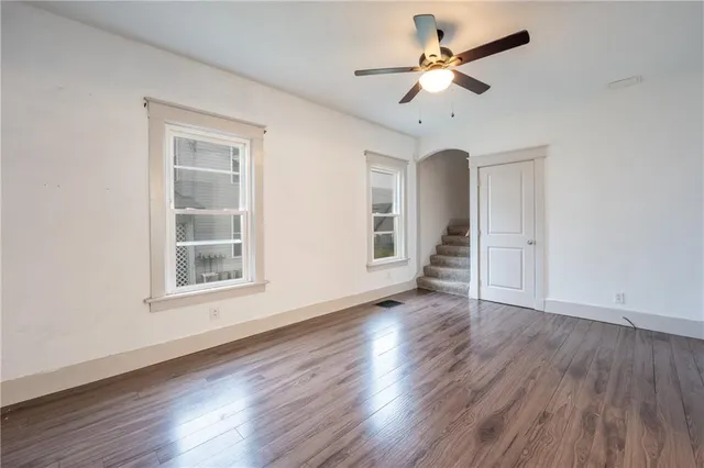 an empty room with wooden floor chandelier fan and windows
