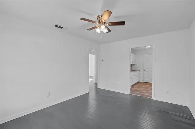 a view of an empty room with wooden floor and a ceiling fan