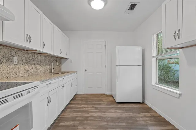 a kitchen with granite countertop white cabinets white appliances a sink and a window