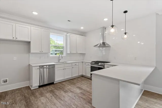 a kitchen with stainless steel appliances granite countertop a sink a stove a refrigerator and white cabinets with wooden floor