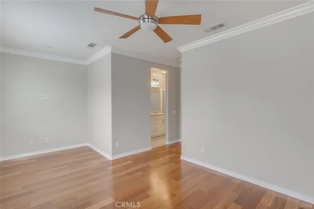 a view of an empty room with wooden floor and a ceiling fan