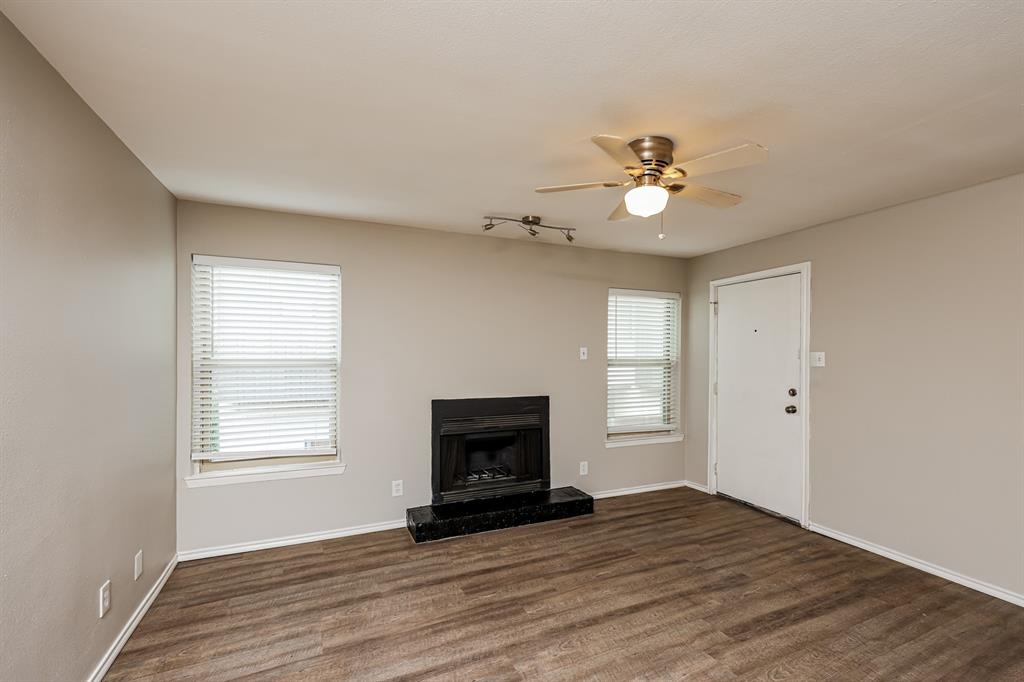 4622 Monarch Street, Unit 202 Dallas, TX 75204 - Photo 7 of 16 Living area featuring a fireplace with a dark stone hearth, wood-finish flooring, two windows with blinds, a ceiling fan, and a track lighting fixture