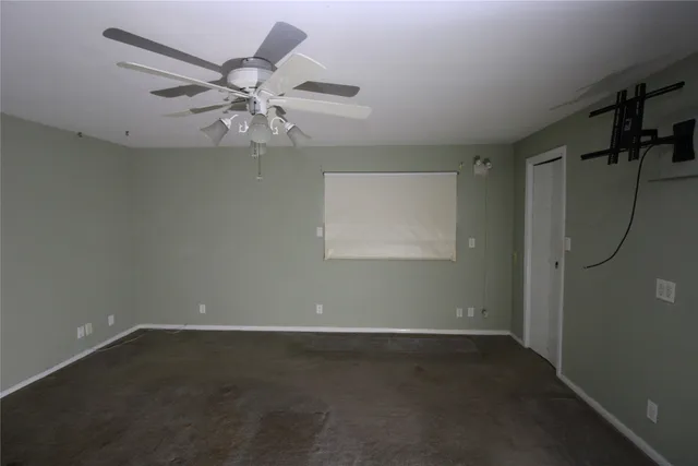 an empty room with chandelier fan and windows