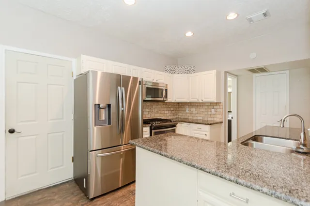 a kitchen with stainless steel appliances granite countertop a refrigerator a stove and a sink with wooden floor