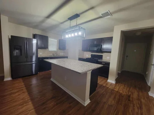 a kitchen with granite countertop a refrigerator a stove top oven and wooden floor