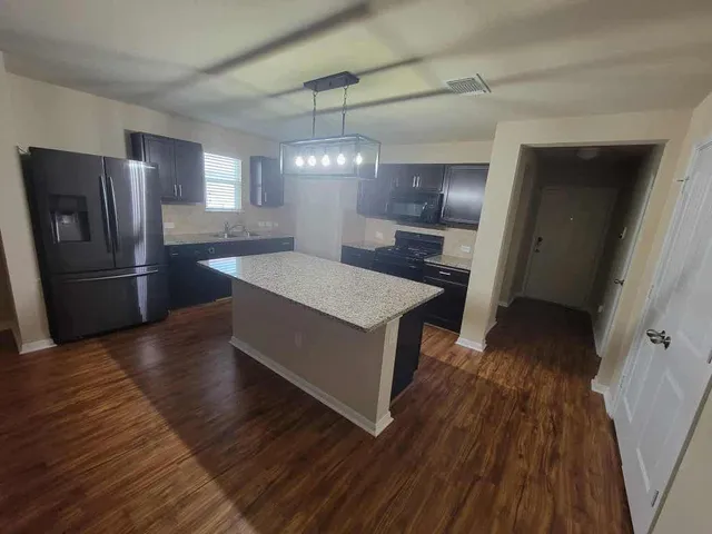 a kitchen with stainless steel appliances granite countertop a refrigerator a sink dishwasher a stove and white countertops with wooden floor