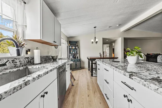 a kitchen with granite countertop a refrigerator oven a sink a stove and white cabinets