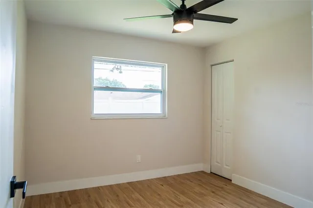 an empty room with wooden floor fan and windows