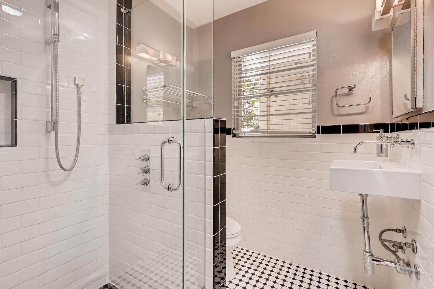 446 Pike Road San Antonio, TX 78209 - Photo 15 of 28 Modern bathroom featuring sleek white subway tiles, a glass-enclosed shower, and distinctive black and white hexagonal floor tiling.