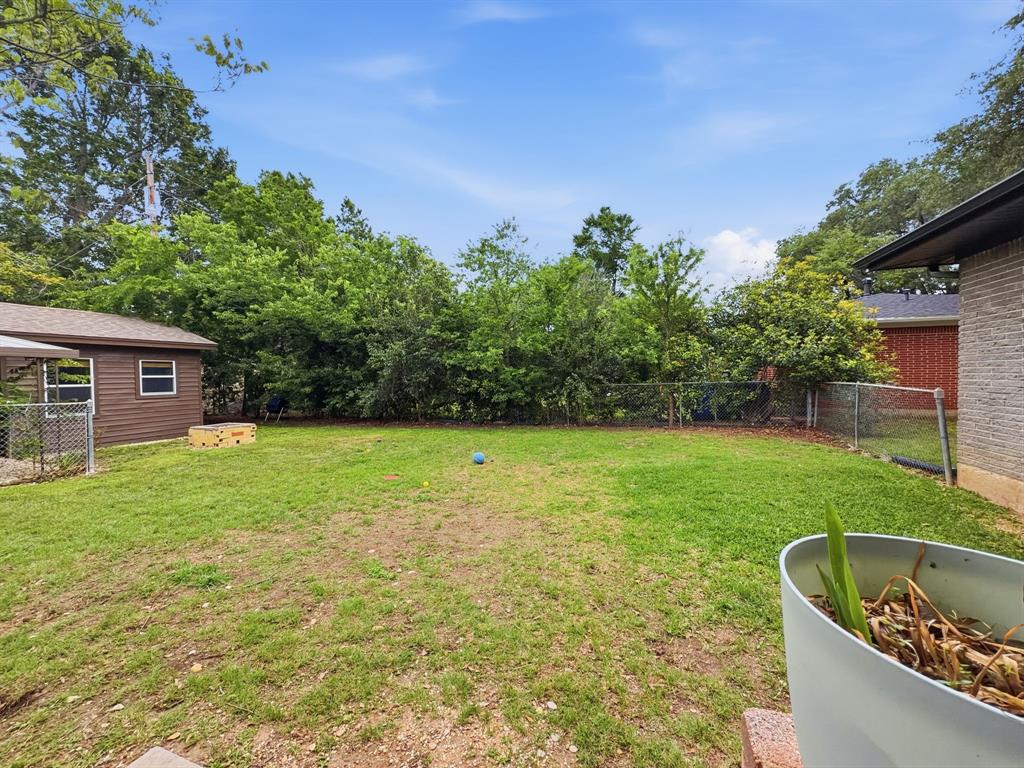 2137 Lenamon Street Waco, TX 76710 - Photo 24 of 29 Expansive backyard featuring a lush green lawn, mature perimeter trees, a chain-link fence, and a detached shed with brown siding and a shingle roof