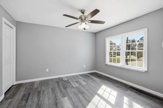 an empty room with wooden floor fan and windows