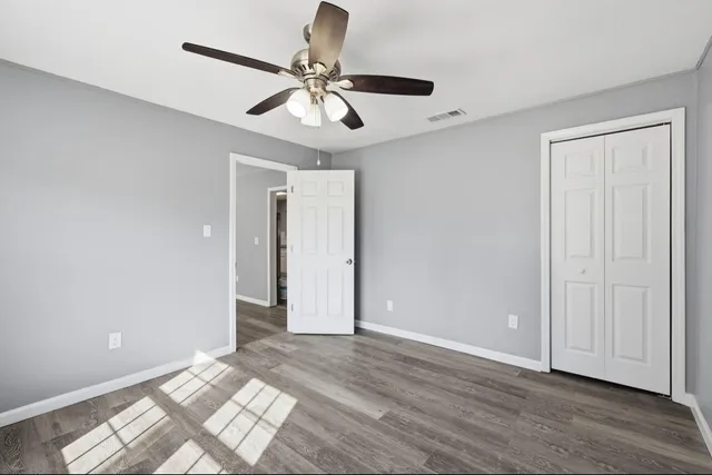 a view of an empty room with wooden floor and a ceiling fan