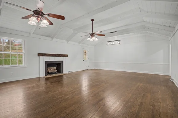 an empty room with wooden floor chandelier fan and windows
