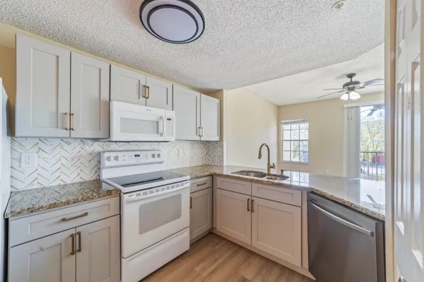 a view of an empty room with wooden floor and a kitchen