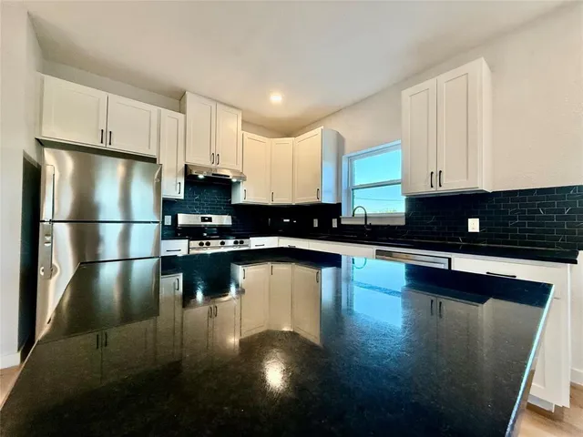 a kitchen with stainless steel appliances a refrigerator a stove a sink cabinets and a wooden floor