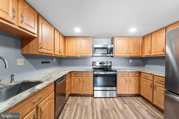 a kitchen with stainless steel appliances granite countertop wooden cabinets a sink dishwasher a stove and a refrigerator with wooden floor