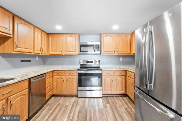 a kitchen with stainless steel appliances granite countertop a refrigerator a sink dishwasher a stove and white countertops with wooden floor