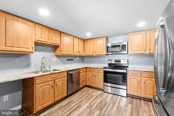 a kitchen with stainless steel appliances granite countertop wooden cabinets a sink a stove a refrigerator with grey cabinets and wooden floor