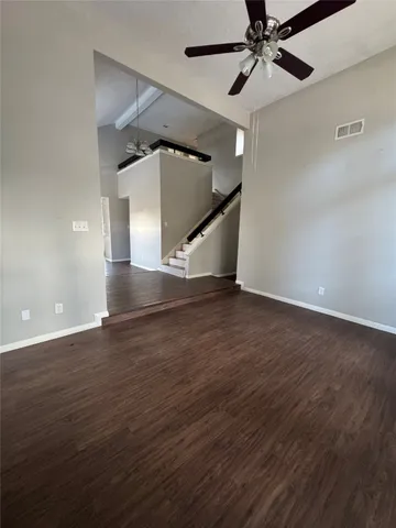 a view of an empty room with wooden floor and a ceiling fan