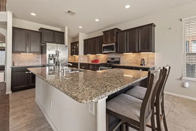 a kitchen with granite countertop kitchen island stainless steel appliances sink refrigerator microwave and cabinets