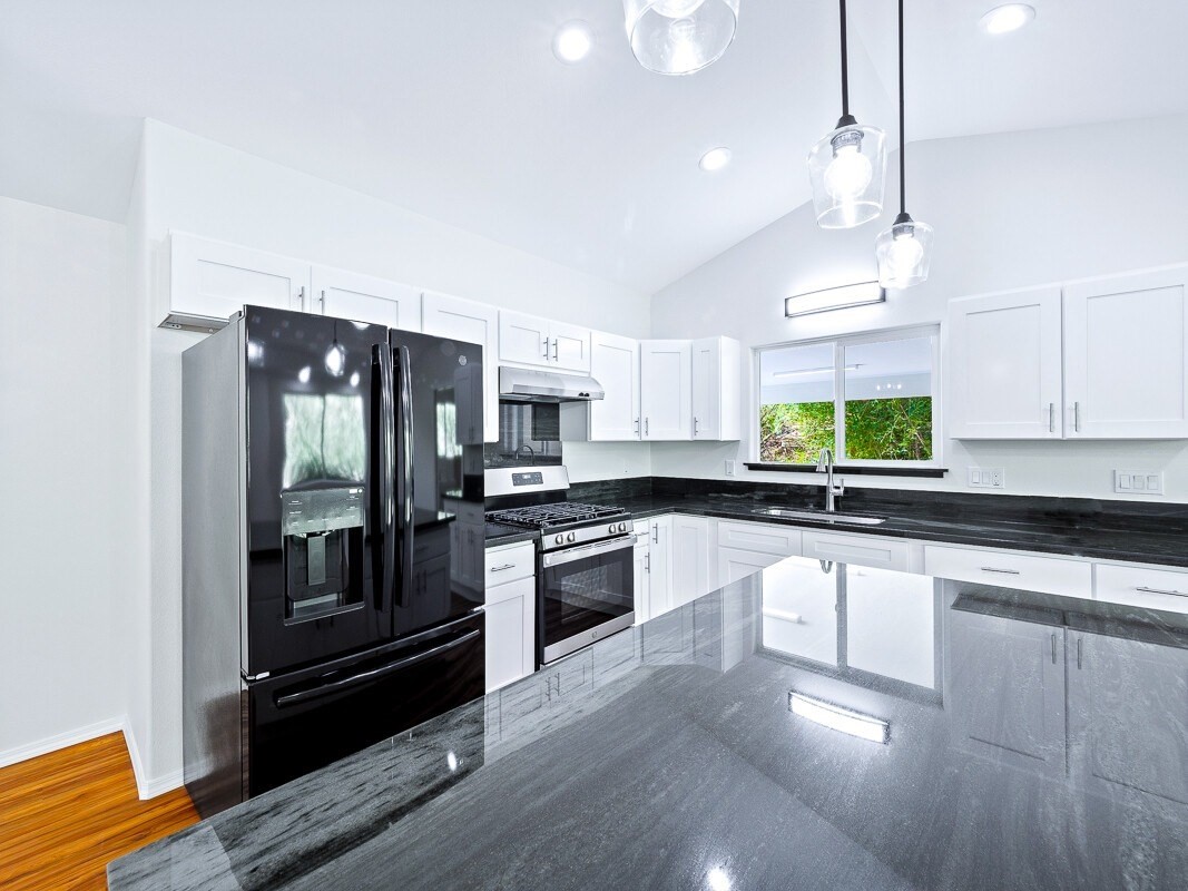 Peleke Road Mountain View, HI 96771 - Photo 7 of 24 a kitchen with stainless steel appliances granite countertop a refrigerator a sink dishwasher a stove and white cabinets with wooden floor