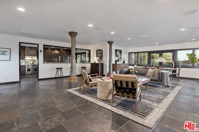 a living room with furniture a rug kitchen view and a large window
