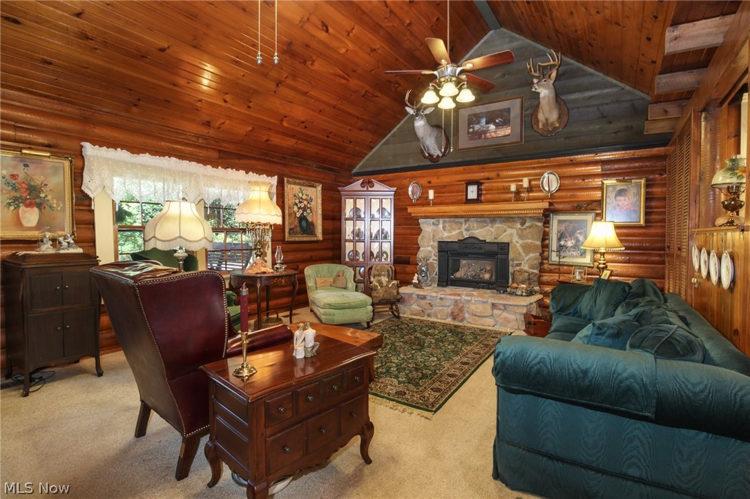 Living room with vaulted ceiling, ceiling fan, a stone fireplace, wood ceiling, and log walls