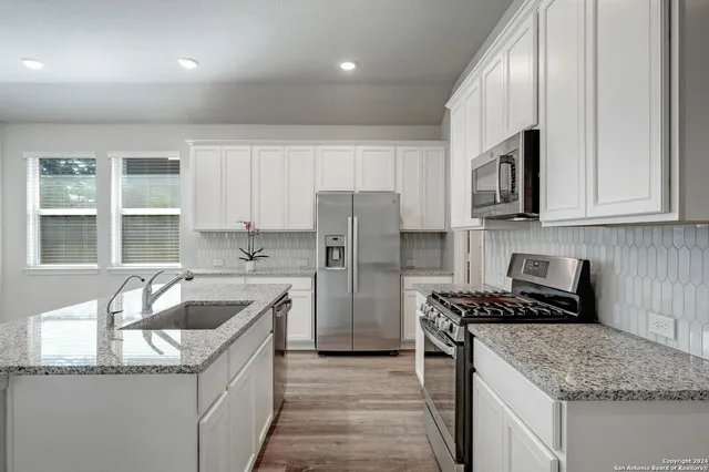 a kitchen that has a sink cabinets counter space stainless steel appliances and windows