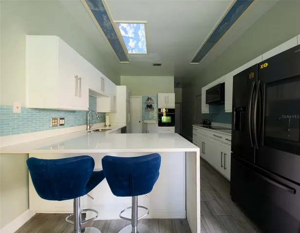 a kitchen with stainless steel appliances granite countertop a sink a stove a refrigerator cabinets and chairs