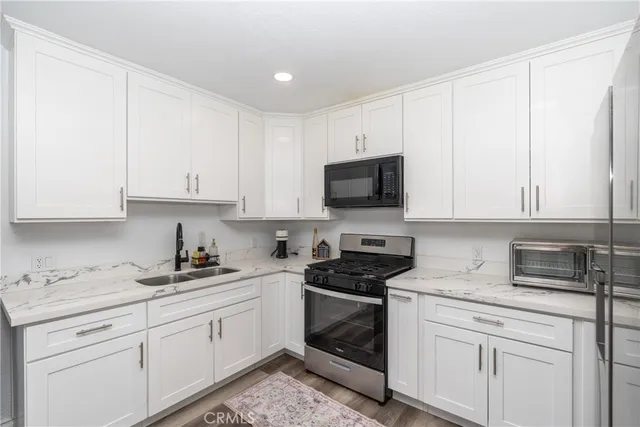 a kitchen with stainless steel appliances a refrigerator a stove top oven a sink and white cabinets with wooden floor