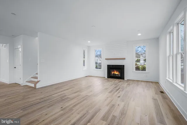 a view of an empty room with wooden floor fireplace and a window