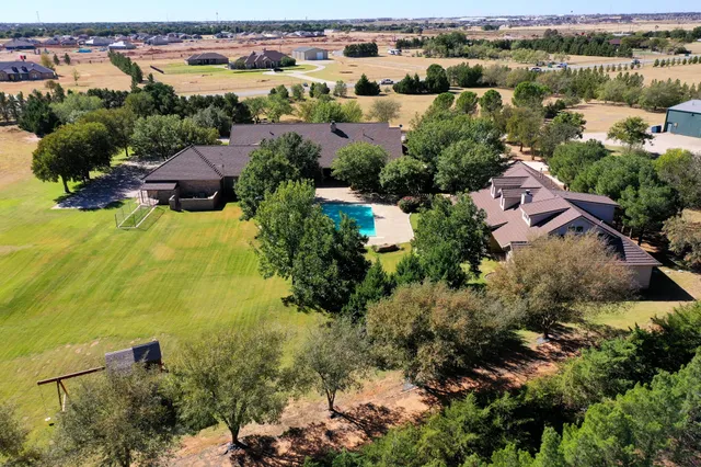 an aerial view of a house with large trees and lake view