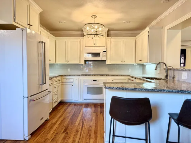 a kitchen with granite countertop wooden floors white cabinets and stainless steel appliances