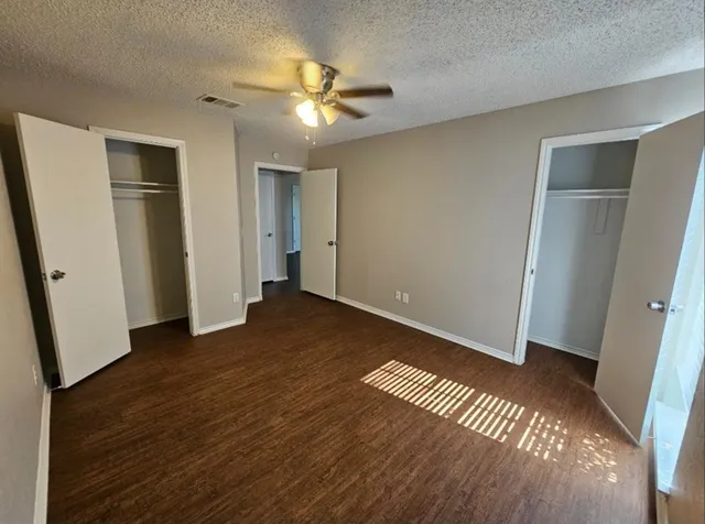 a view of an empty room with wooden floor and a ceiling fan