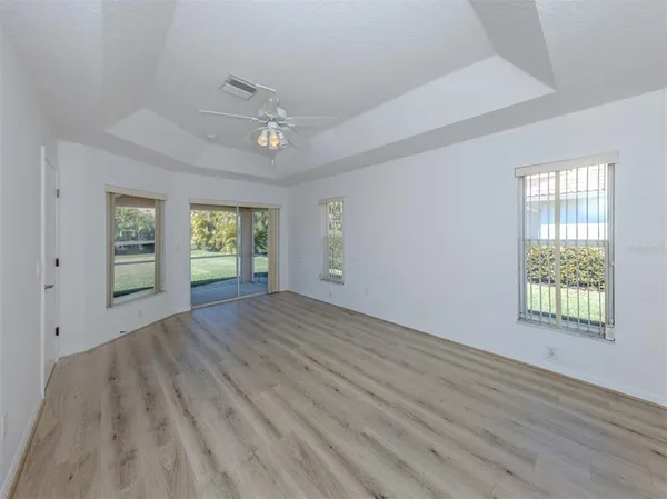an empty room with wooden floor fan and windows