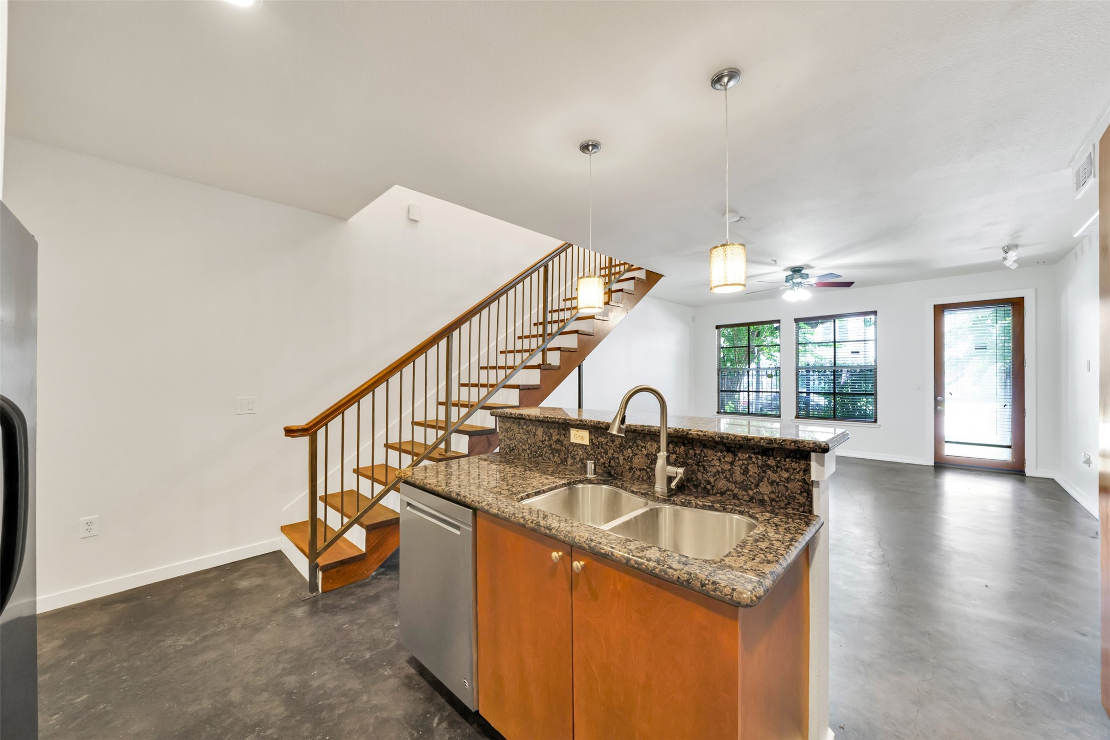 Inviting open-concept living space highlighting modern floating stairs, polished concrete floors, granite-topped bar seating, and contemporary pendant lighting, with seamless flow to the living area and direct access to the patio, where the vibrant Midtown awaits.