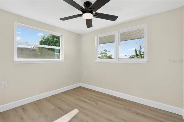 a view of an empty room with wooden floor and a ceiling fan