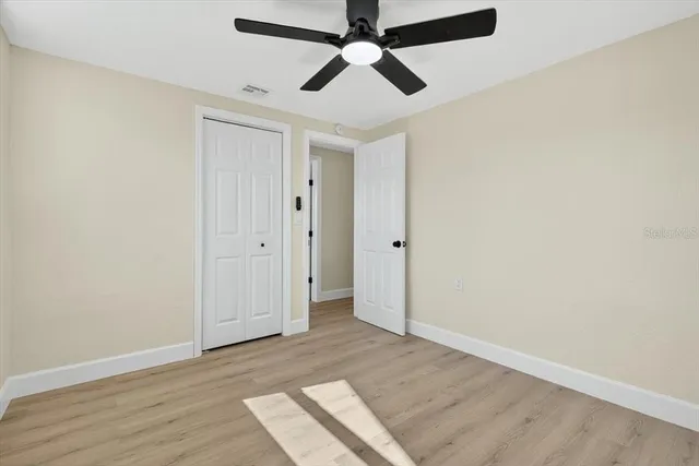 an empty room with wooden floor ceiling fan and windows