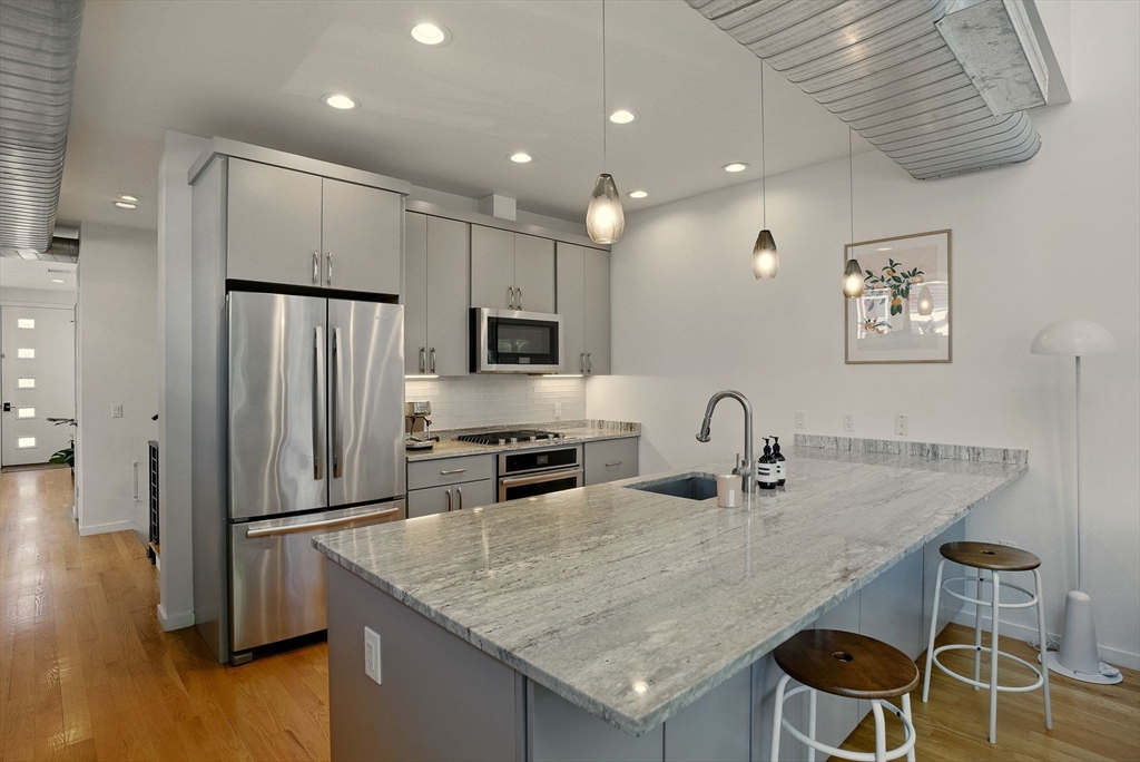 151 Sherman Street Cambridge, MA 02140 - Photo 12 of 35 a kitchen with stainless steel appliances granite countertop a table chairs stove refrigerator and wooden floor
