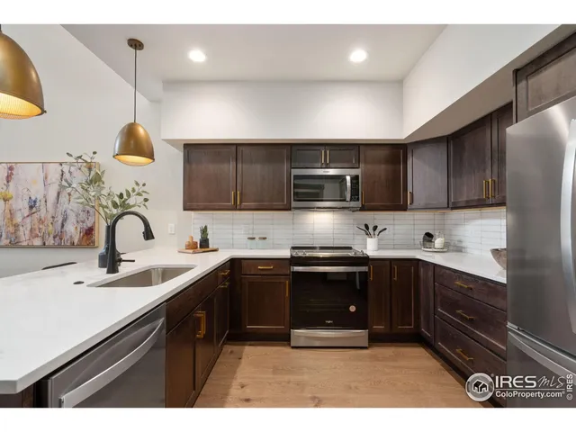 a kitchen with stainless steel appliances granite countertop a sink a refrigerator and a wooden floor