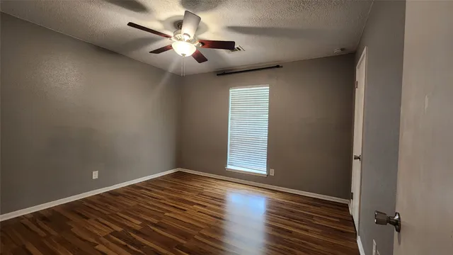 an empty room with wooden floor chandelier fan and windows