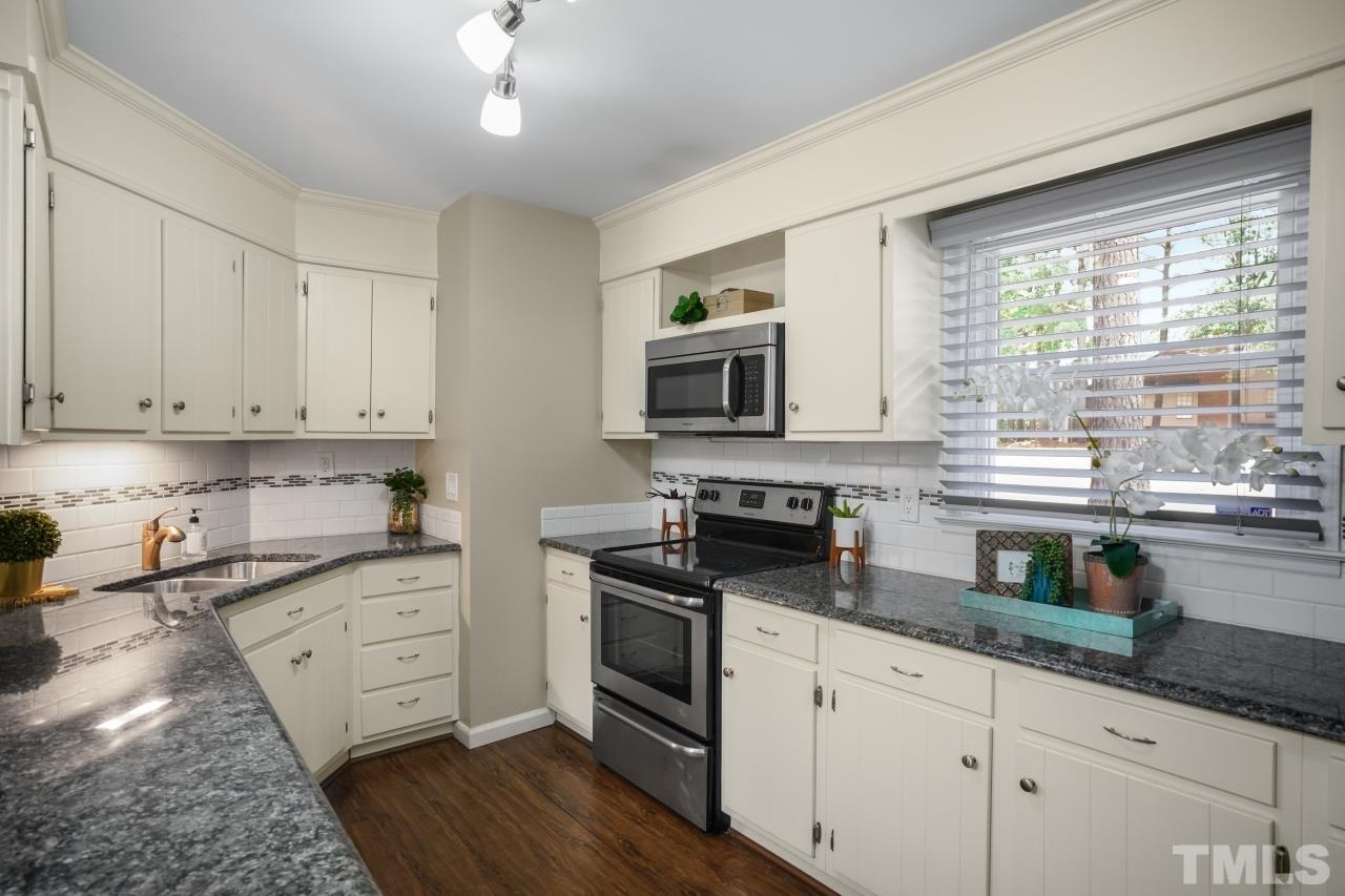 7016 Ray Road Raleigh, NC 27613 - Photo 4 of 26 a kitchen with granite countertop a stove a sink and white cabinets