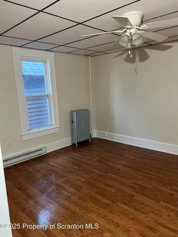 an empty room with wooden floor chandelier fan and windows