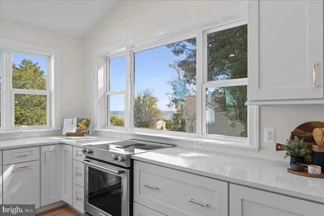 a kitchen with stainless steel appliances a stove a sink a refrigerator white cabinets and couches with wooden floor