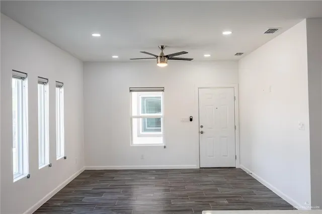 an empty room with wooden floor ceiling fan and windows