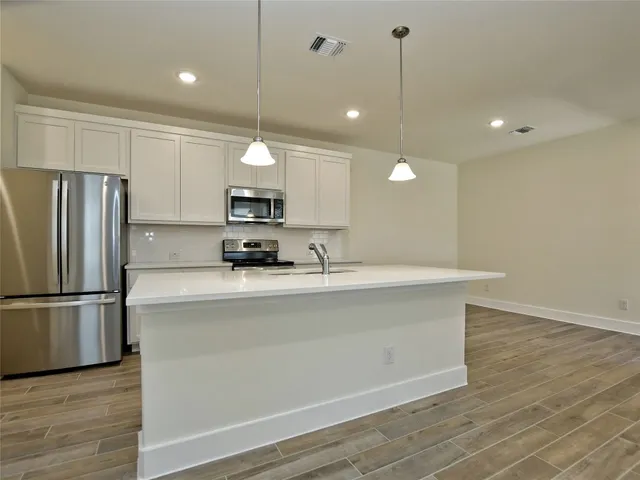 a kitchen with stainless steel appliances granite countertop a refrigerator a sink dishwasher a stove and a refrigerator with wooden floor