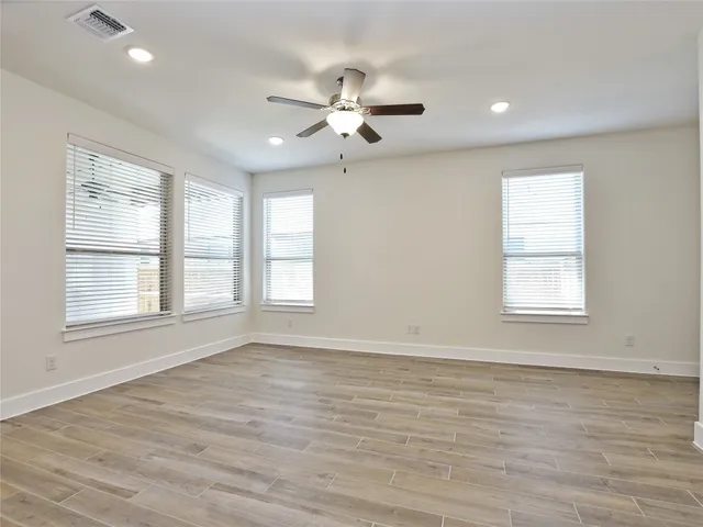 an empty room with wooden floor ceiling fan and windows